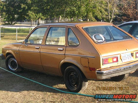 Brown hatchback car, side view, with a dent on the rear quarter panel and a circular decal on the rear window