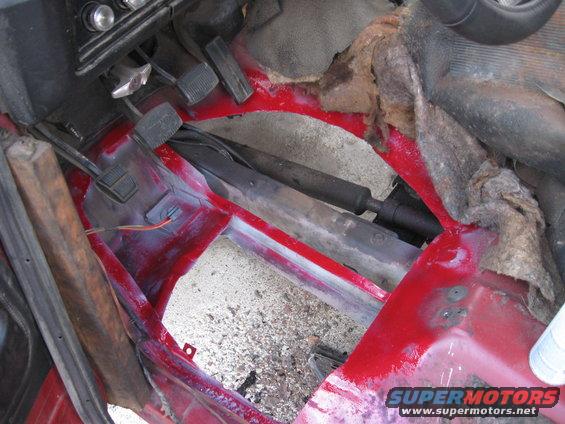 1981 Ford Bronco interior floor with red paint and exposed metal, showing pedals and drive shaft
