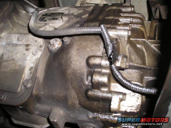 Transmission housing with oil leaks and a metal tag. A wire harness is attached with tape