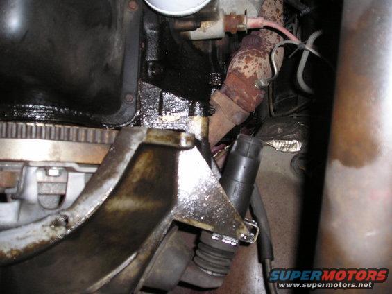Close-up of engine components with visible oil leaks and rust on exhaust manifold