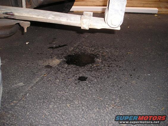 Undercarriage of a vehicle with a fluid leak on asphalt. Leaf spring visible