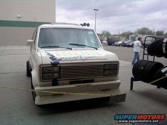 White van with a colorful stripe decal on the hood, parked in front of a building