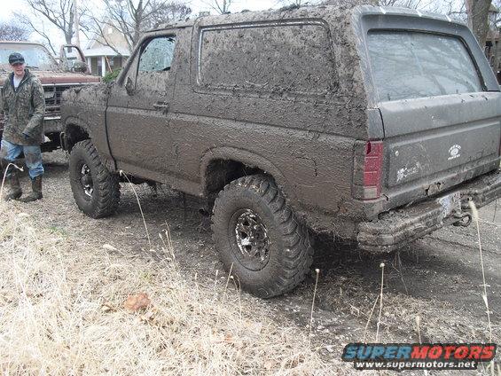 Mud-covered 1986 Ford Bronco parked next to a brown truck. A person stands by the truck