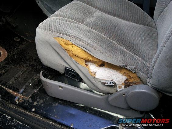 Torn gray fabric car seat with exposed yellow foam and white stuffing, showing a "LIFT" lever
