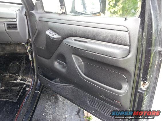 Black interior door panel with armrest and window controls, showing exposed wiring and bare floor