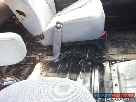 Interior of a vehicle showing worn fabric seats and a dirty floor with seatbelt hardware