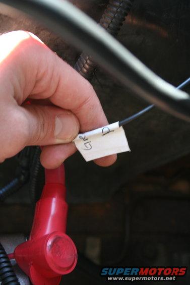 Hand holding white label with 'GR' and 'D' written on it, attached to a wire near a red battery terminal