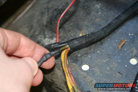 Hand connecting a black wire to a bundle of wires, some yellow and red, with black electrical tape