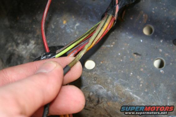 Hand holding damaged wire from a wiring harness with red, yellow, and green wires visible