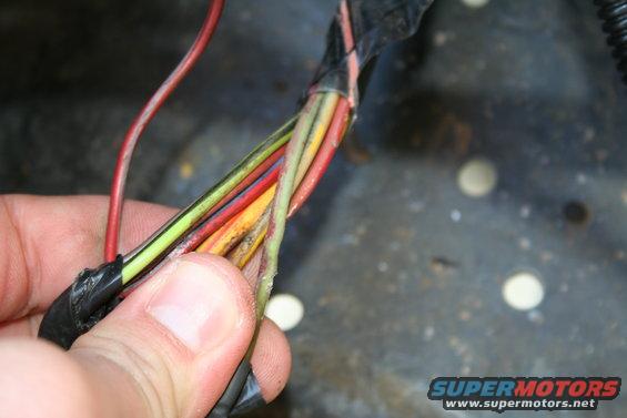 Close-up of a hand holding a damaged wiring harness with multiple colored wires
