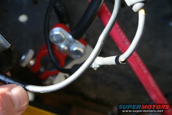 Close-up of car battery terminal connections and wiring. A red cable is visible