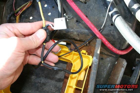 Hand holding black and yellow wires with a fuse holder, connected to red and white cables