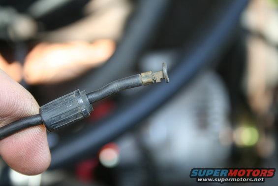 Hand holding a black electrical cable with a metal connector at the end, blurred engine components in background