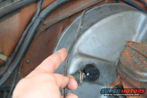 Finger pointing at vacuum hose near brake booster and master cylinder