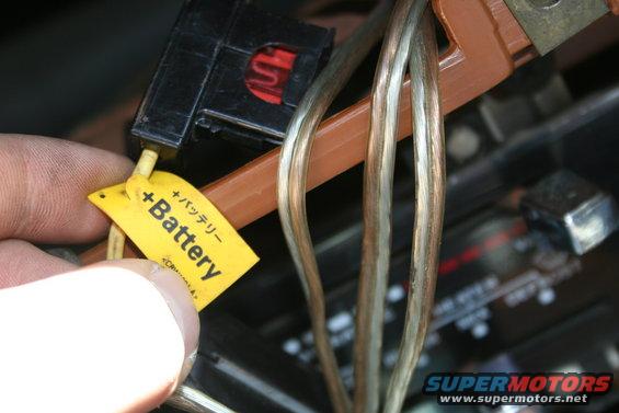 Hand holding yellow tag labeled '+ Battery' attached to wires near a black connector