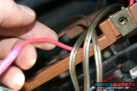 Close-up of a hand holding a pink wire near a brown plastic harness with multiple grey wires