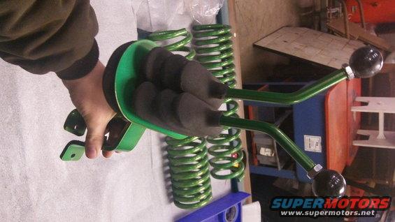 Person holding green suspension part with black grips, green coil springs in background
