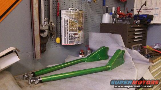 Pair of green metal suspension control arms with rod ends on a workbench