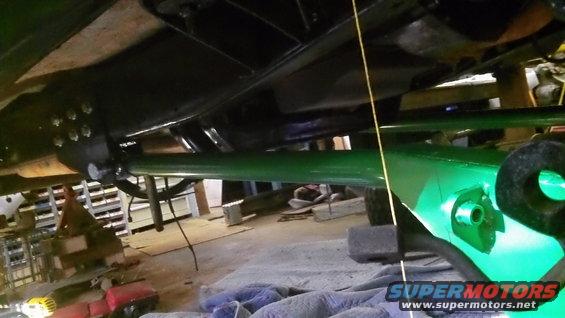 Close-up of green painted suspension arm and black frame components under a vehicle