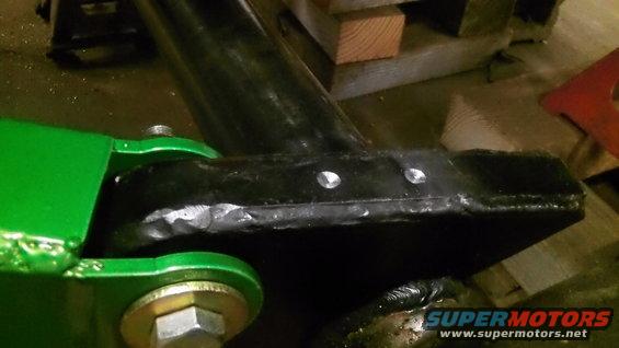 Close-up of a green suspension part bolted to a black metal component with two visible bolts