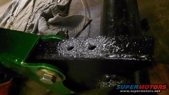 Green painted metal bracket attached to a black metal component covered in metal shavings and two drilled holes