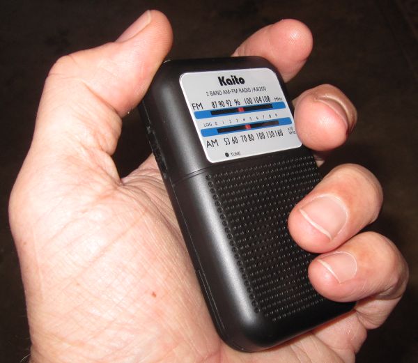 Hand holding a Kaito KA200 AM/FM radio with tuning dial visible
