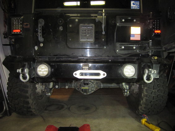 Black Jeep's rear bumper has a white winch, two round lights, and tow hooks. Aftermarket LED tail lights are visible