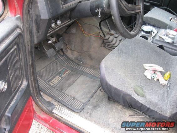 Interior of a 1981 Ford Bronco showing floor mats with Ford logo, pedals, steering wheel, and seat