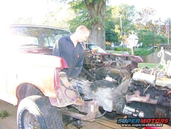Man working on engine of a red Ford Bronco, front end disassembled
