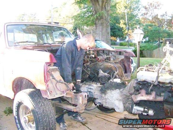 Red Ford Bronco with front end disassembled, engine exposed, mechanic working