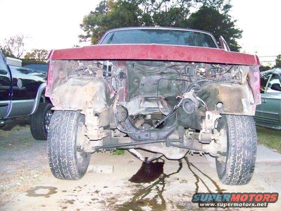 1985 Ford Bronco front clip removed, showing engine bay and chassis components. Another truck is parked to the left