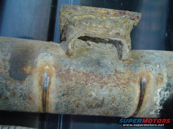 Heavily rusted metal pipe with a welded bracket, showing signs of wear and corrosion