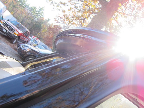 Several vehicles parked outside, including a red truck and a black car. Sun glare is prominent