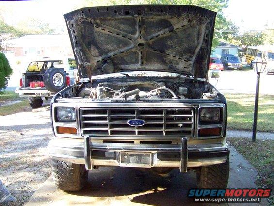 Front view of a Ford truck with hood open, showing engine. Another Ford SUV is parked behind it