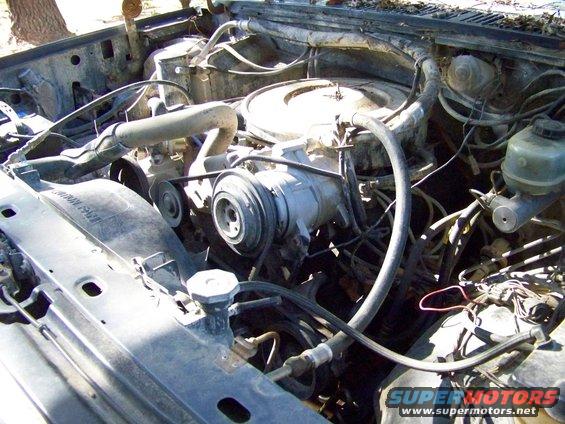 engine bay with AC compressor, radiator, and hoses visible. Some text on fan shroud