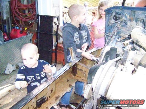 Three children gathered around an open engine bay, one holding a tool