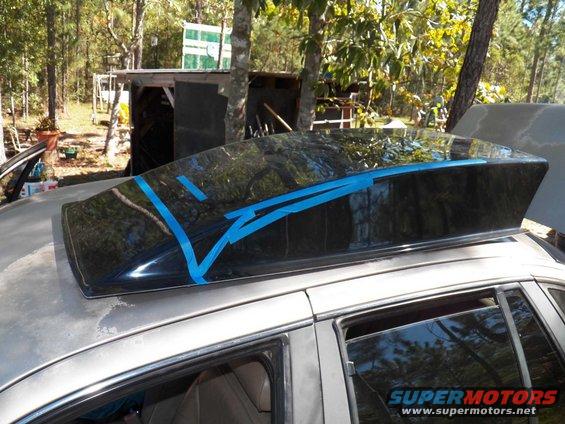 Car roof with a black spoiler held by blue tape. The car is silver and appears to be outdoors