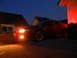 2003 Mercury Marauder - Red Ford Mustang coupe parked in driveway at dusk with headlights on.