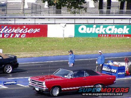 Red 1967 convertible with a black top, seen from the front at a drag strip