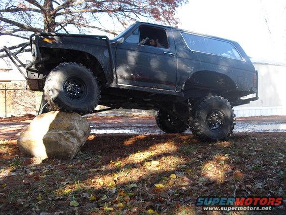 Black lifted Ford Bronco with large tires on a rock, custom bumper, off-road modifications