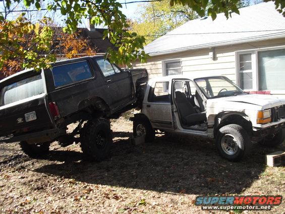 Dark lifted SUV on blocks next to a white damaged SUV with doors removed