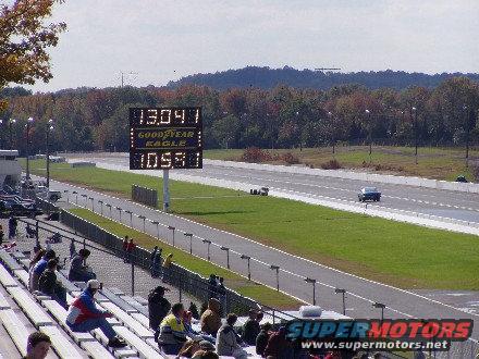 Drag strip with scoreboard showing times, spectators in bleachers, and a car on the track
