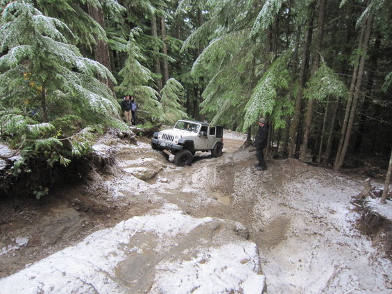 White 2007 Jeep Wrangler navigating a snowy, muddy forest trail