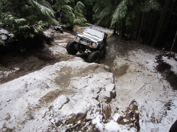 Off-road vehicle with large tires navigating a snowy, wooded trail