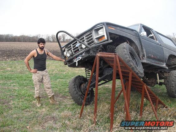 Man standing next to a lifted SUV with a custom bumper and roll cage, front tire on a ramp