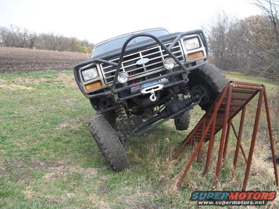 Ford Bronco with a brush guard and winch on uneven terrain, driving up a metal ramp