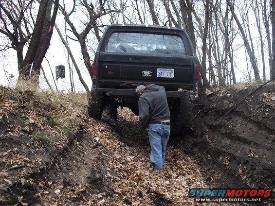 1986 Ford Bronco rear view, off-roading on a muddy trail with a person standing behind it
