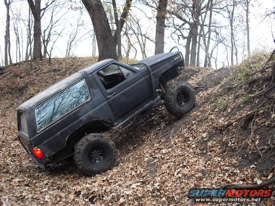 Black SUV with large tires climbing a leaf-covered dirt hill