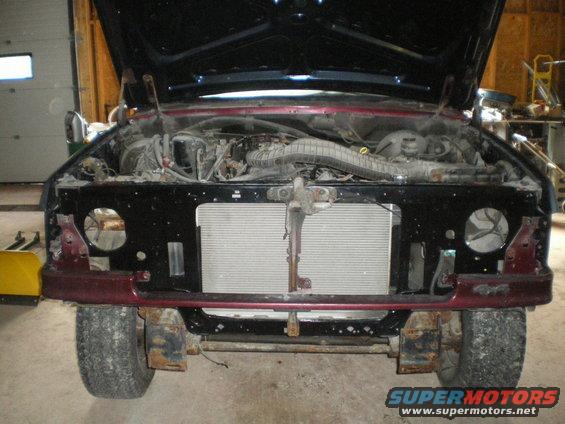 Front view of a disassembled vehicle with hood open, showing engine and radiator