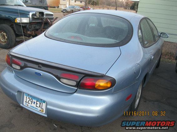 Light blue sedan's rear, showing taillights, spoiler, and Minnesota license plate 129-EXL